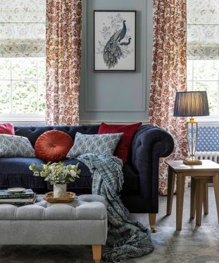 A blue living room with a blue couch, side table with lamp, and a gray storage ottoman